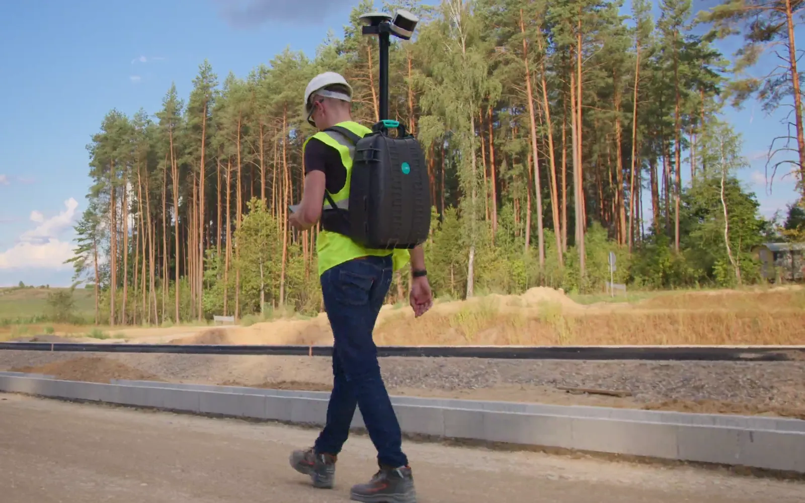 Operator in a helmet and hi-vis vest surveying a road under construction with the BP-32 backpack